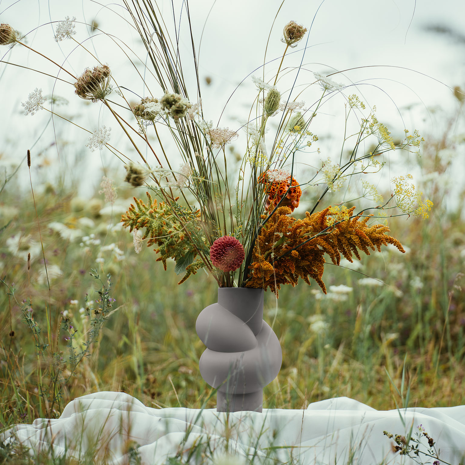 Node Lava avec un bouquet de fleurs automnales se trouve sur une couverture blanche dans un champ de fleurs.